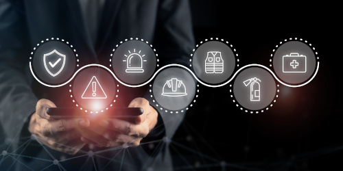 Ein Mann hält ein Smartphone, umgeben von Symbolen für Sicherheit, Alarm, Schutzwesten und Erste-Hilfe.