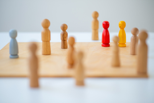 Holzfiguren auf einem Spielbrett, einige stehen in Reihen, zwei Figuren in Rot und Gelb heben sich hervor.