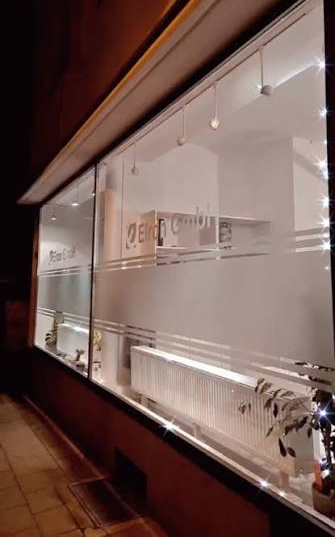 Beleuchtetes Schaufenster eines Ladens mit Milchglasstreifen und weißen Innenräumen bei Nacht