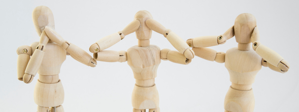 Drei Holzfiguren, die sich die Ohren zuhalten.